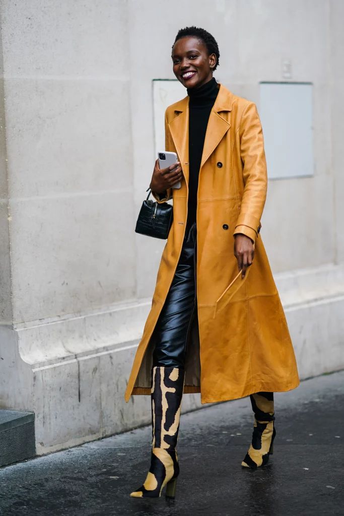 Woman wears yellow leather trench jacket with black turtleneck and leather pants